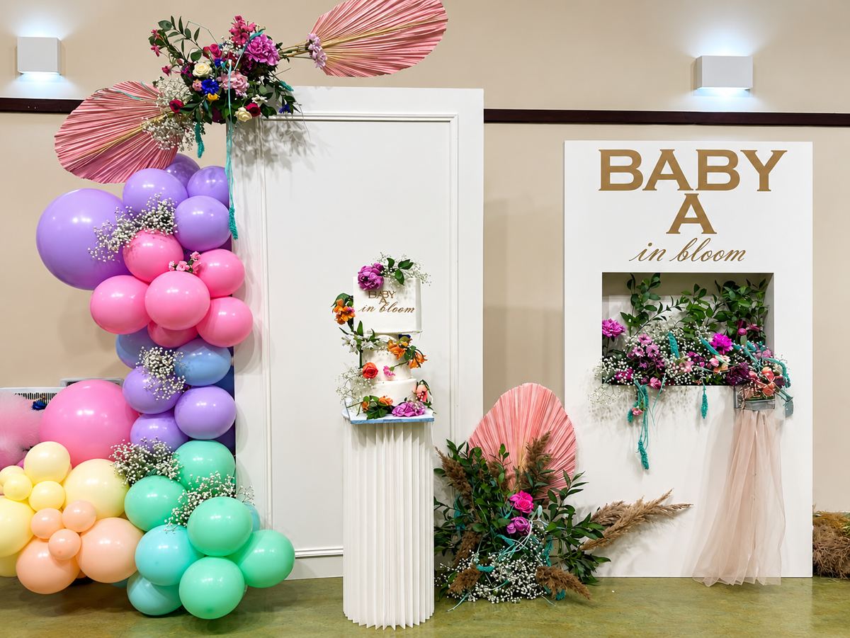 Pastel baby shower setup with balloons, florals and a flower-dressed cake